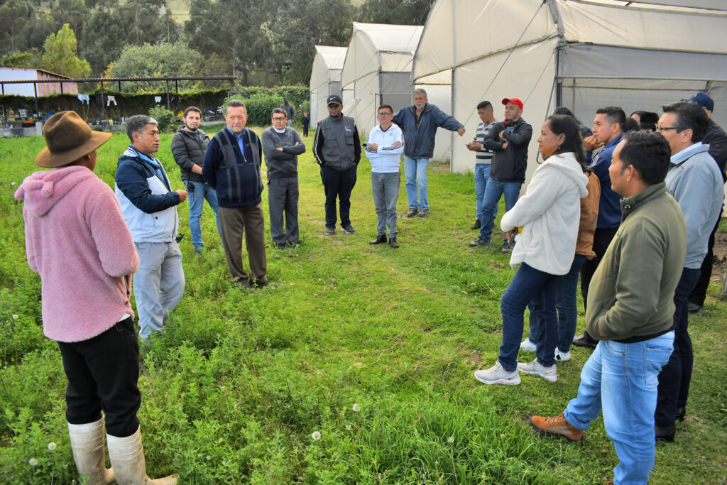 Varias personas reunidas en un campo verde. En el fondo se puede ver varios invernaderos